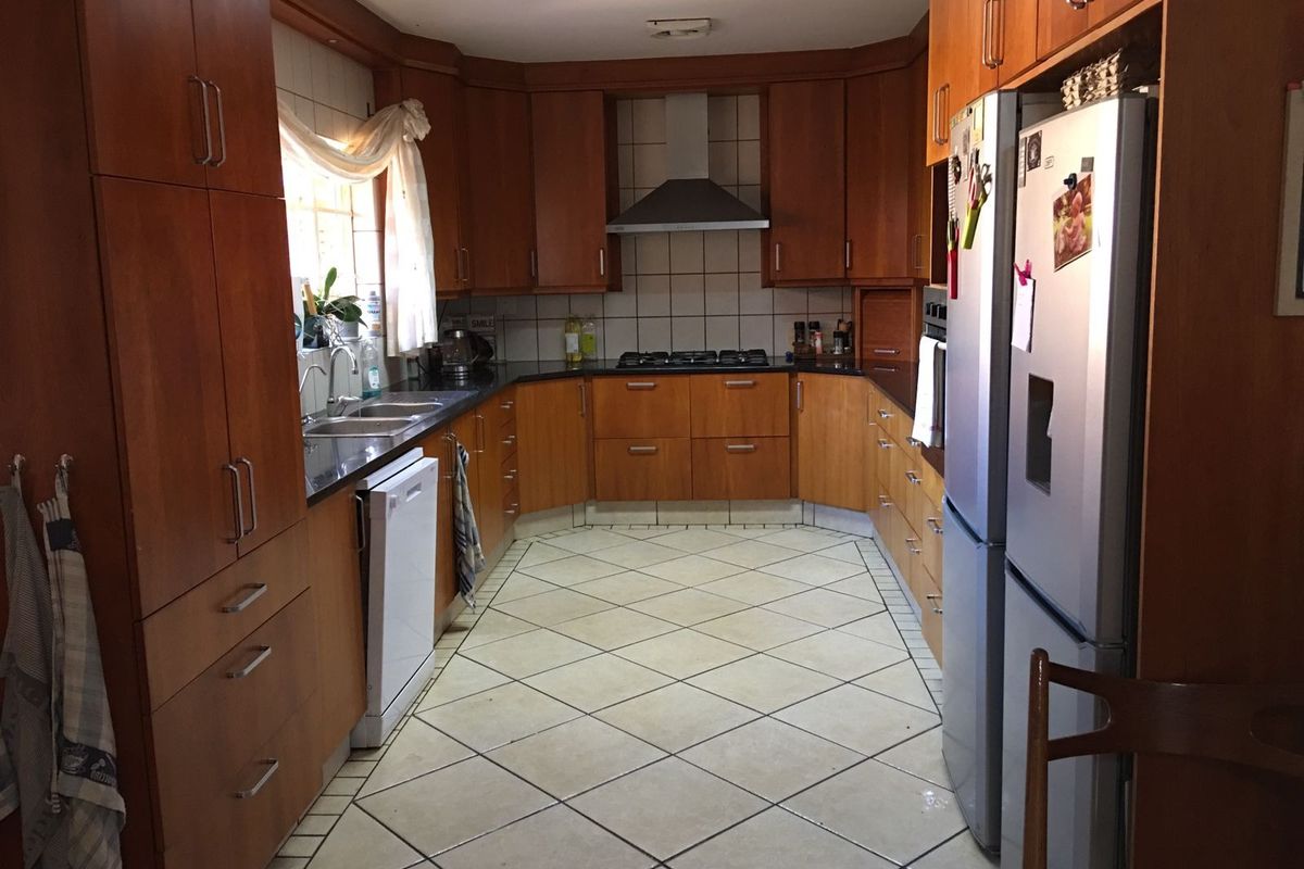 A functional kitchen featuring wooden cabinetry, granite countertops, a built-in gas hob with extractor fan, and tiled flooring.