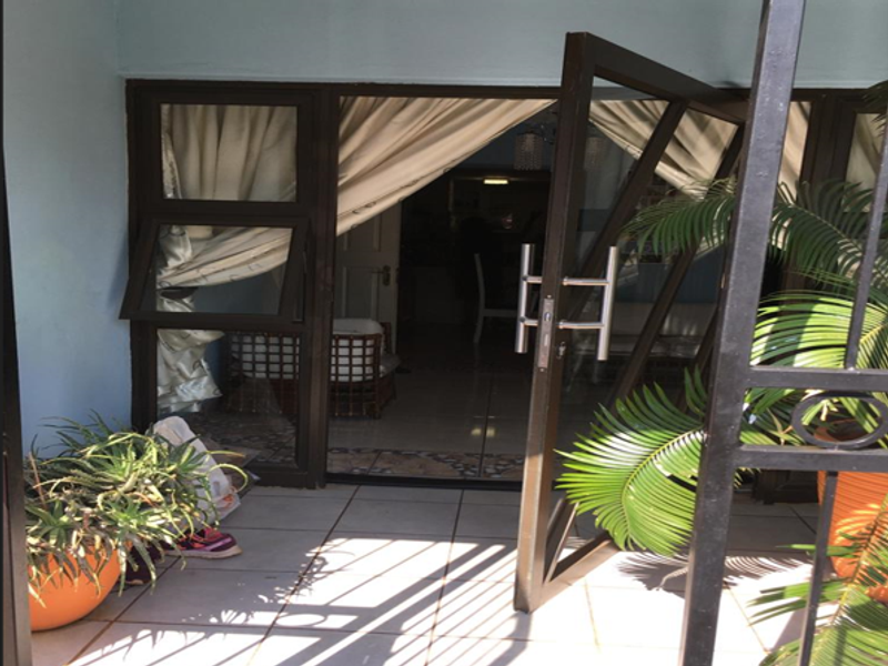A covered patio area featuring tiled flooring and a large metal-framed glass door leading into the interior living space.