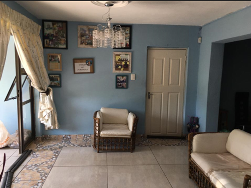 A living room featuring tiled flooring with decorative border accents, a central chandelier, and access to an outdoor area through a sliding glass door.