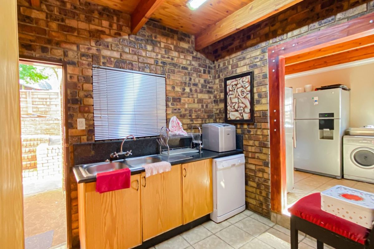 A rustic kitchen area featuring exposed brick walls, timber ceiling beams, and a functional sink unit with adjacent laundry access.