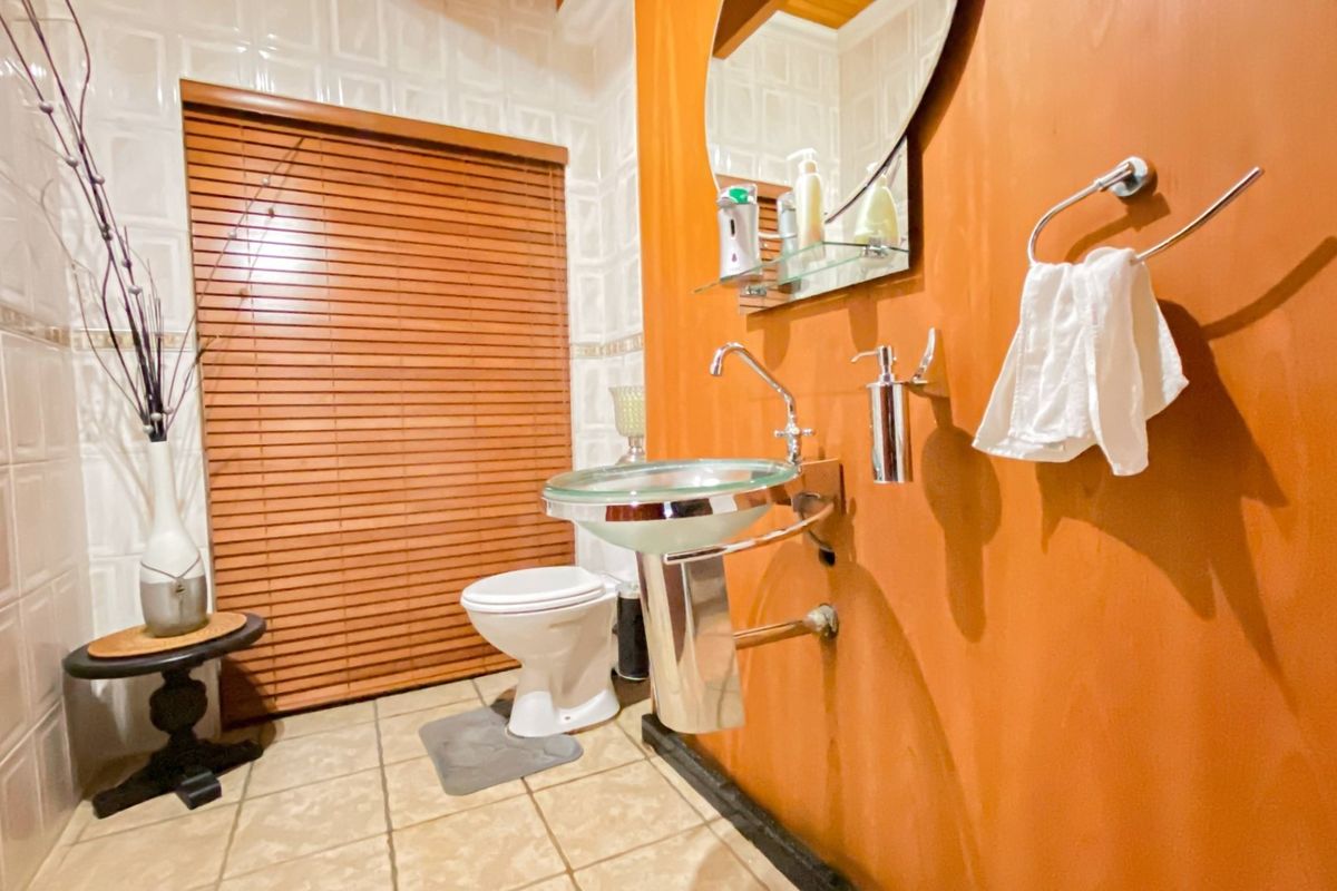 A compact bathroom featuring a wall-mounted glass vessel sink, ceramic toilet, and tiled walls with a wooden blind covering the window.