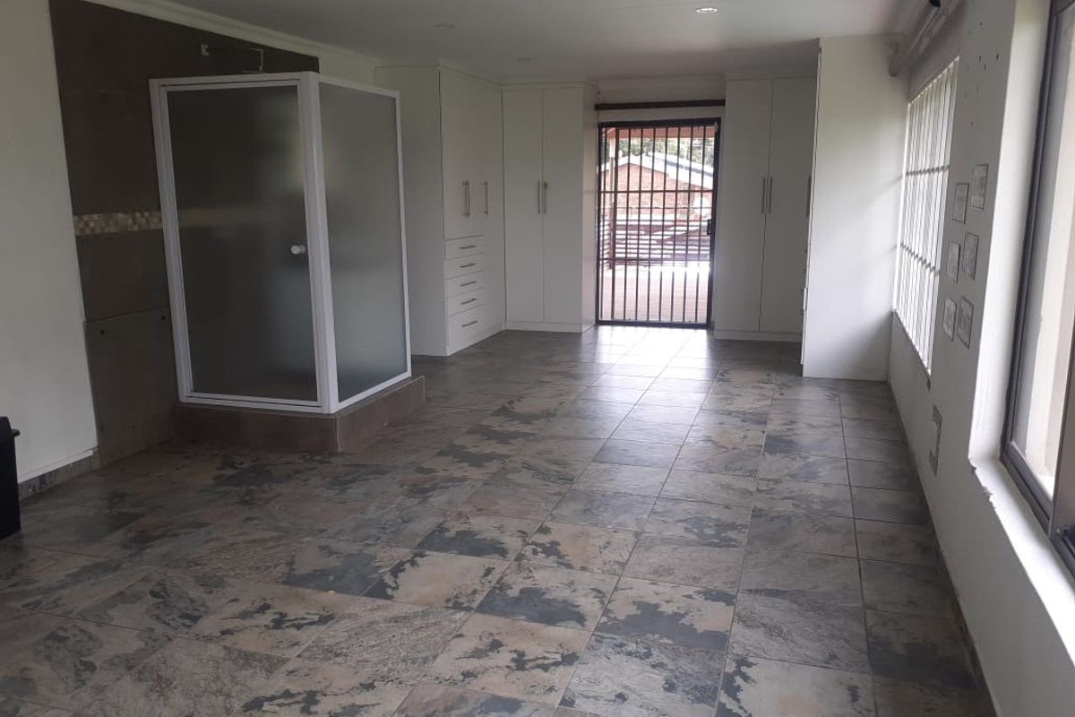 Spacious bedroom featuring built-in cupboards, an en-suite shower cubicle, tiled flooring, and direct access to an outdoor area through a security gate.