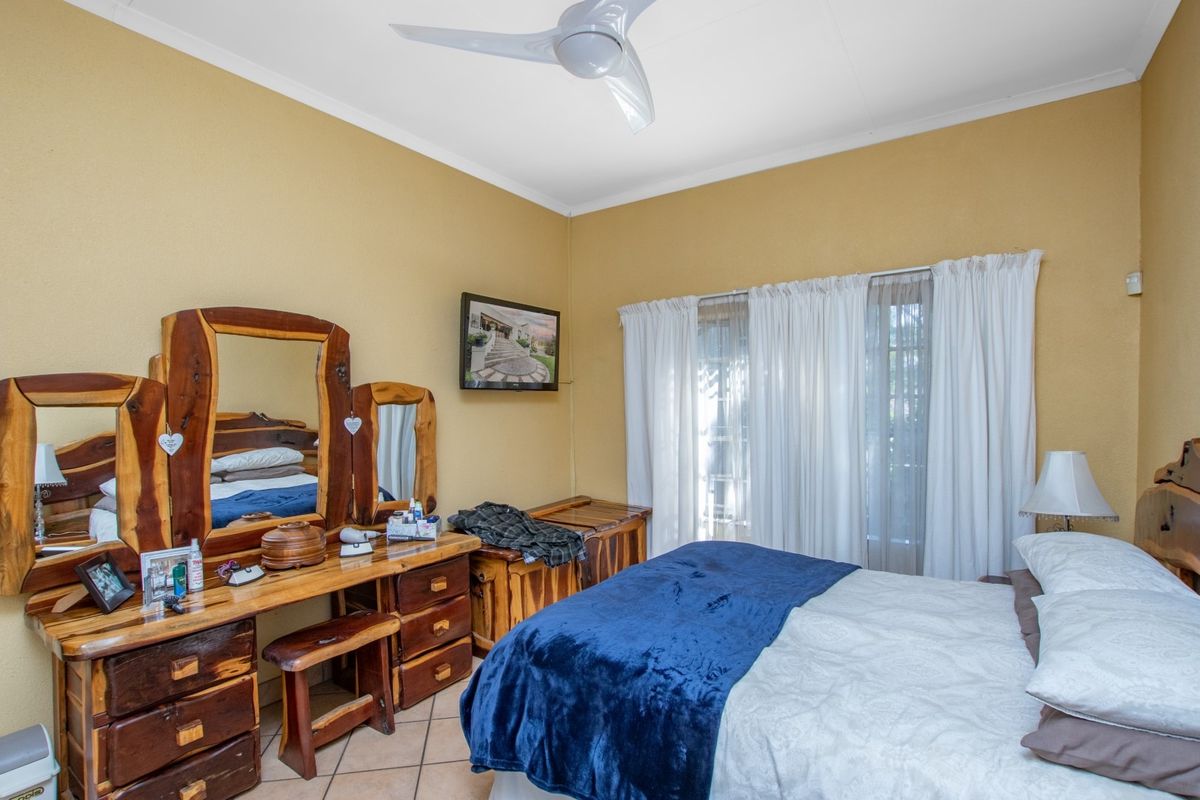 A bedroom featuring tiled flooring, a ceiling fan, and large windows with curtains, providing a functional and comfortable living space.