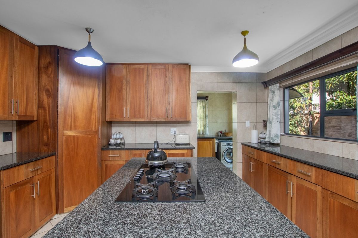 A functional kitchen featuring wooden cabinetry, granite countertops, a central island with a built-in gas hob, and an adjacent scullery area.