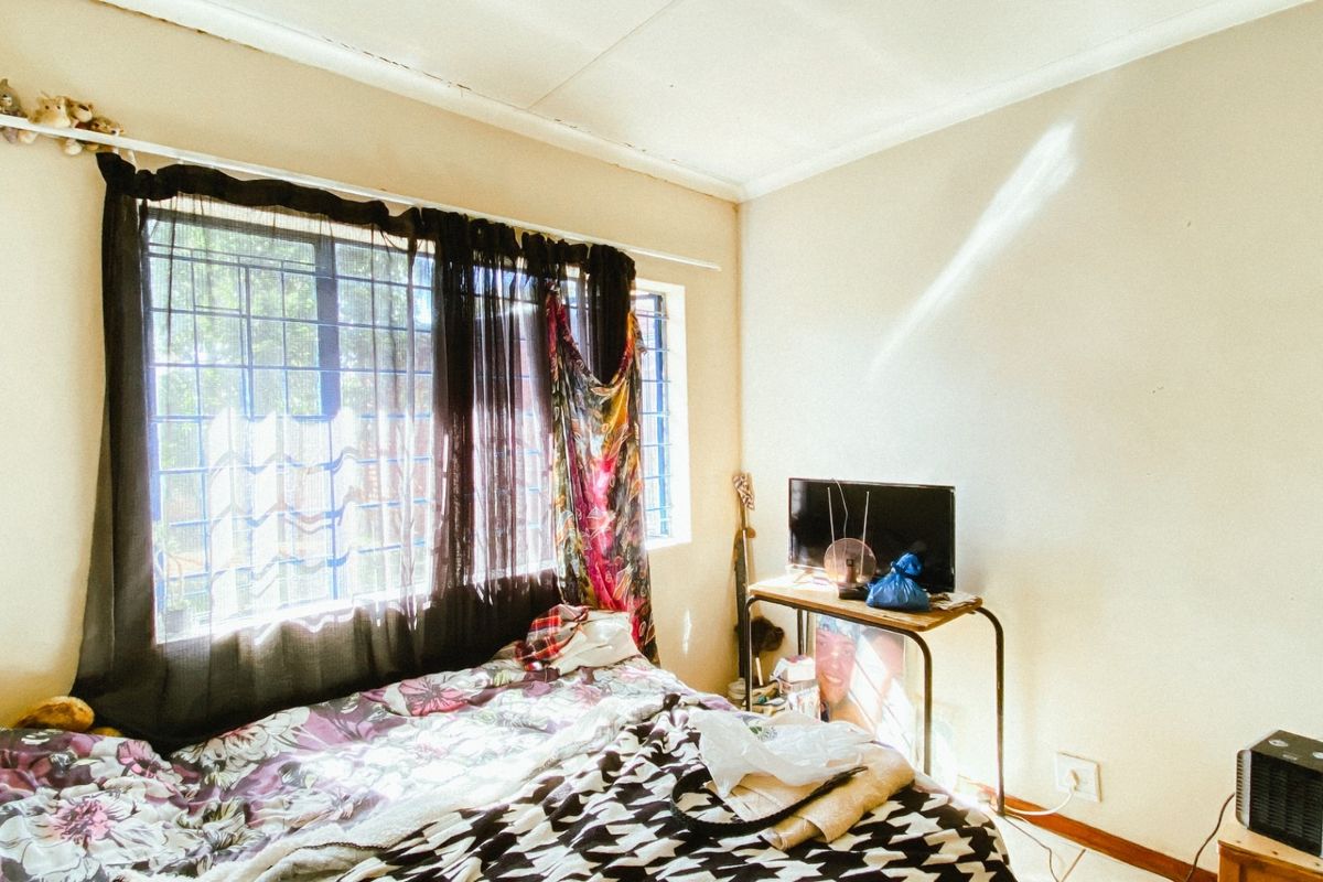 A bedroom featuring a large window with security bars, standard ceiling finish, and electrical outlets.