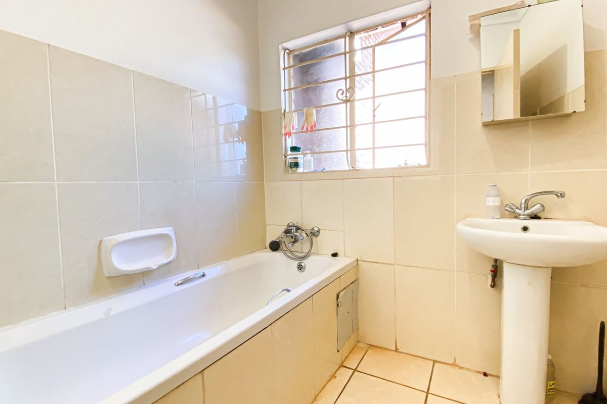 A functional bathroom featuring a built-in bathtub, pedestal sink, and tiled walls, offering a neutral canvas for potential cosmetic updates.