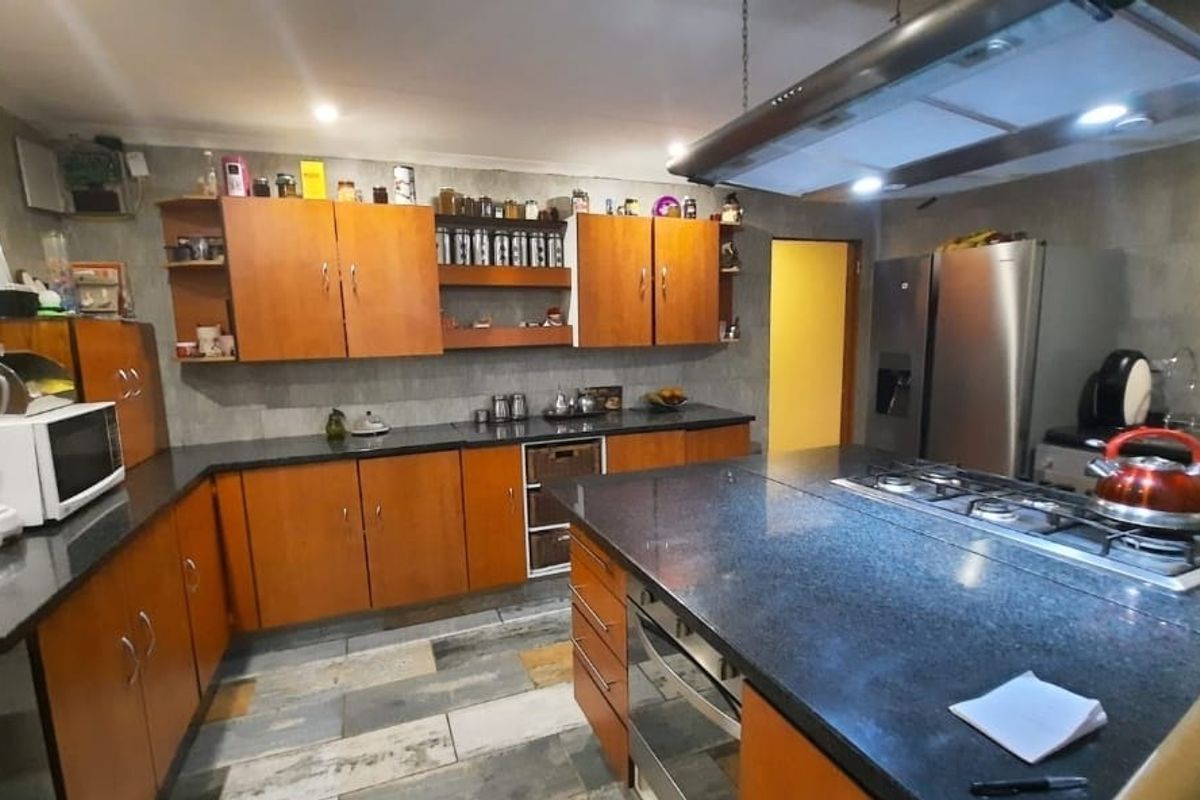 Spacious kitchen featuring wooden cabinetry, granite countertops, a central island with a built-in gas hob, and an overhead extractor fan.