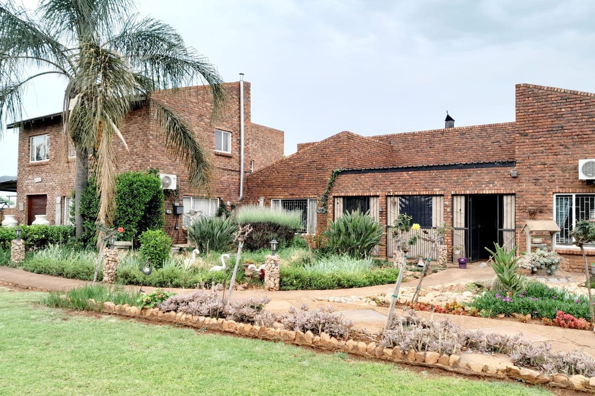 A view of the rear exterior of a face-brick small holding, featuring established garden landscaping and paved pathways leading to the main dwelling.