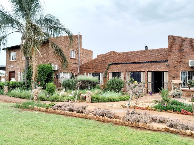 A view of the rear exterior of a face-brick small holding, featuring established garden landscaping and paved pathways leading to the main dwelling.