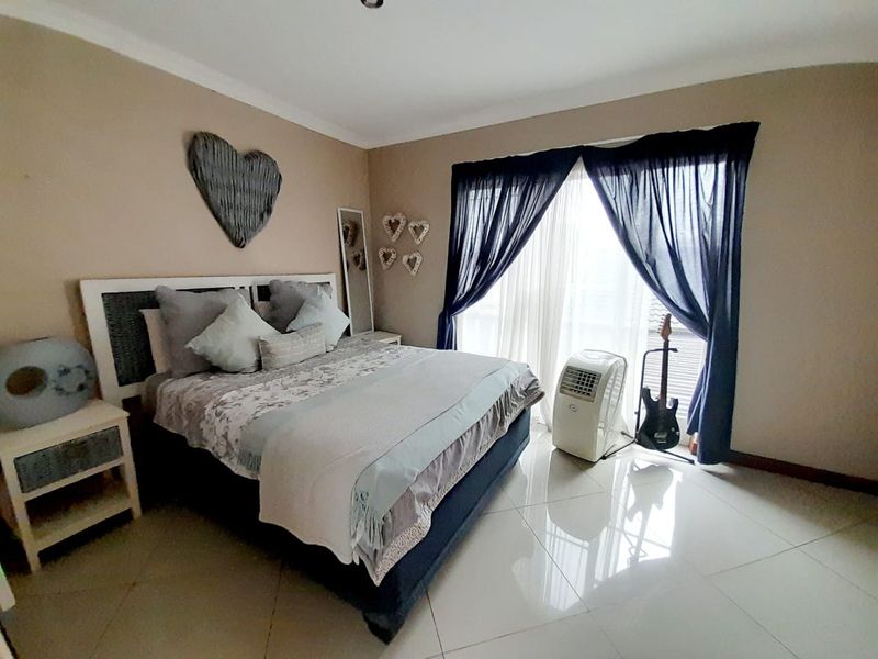 A well-lit bedroom featuring large format floor tiles, neutral wall tones, and a sliding door providing access to the exterior.
