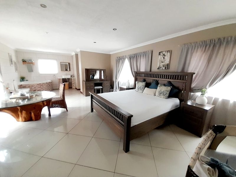 Spacious open-plan bedroom suite featuring tiled flooring, integrated en-suite bathroom area with a corner bathtub, and large windows allowing for natural light.