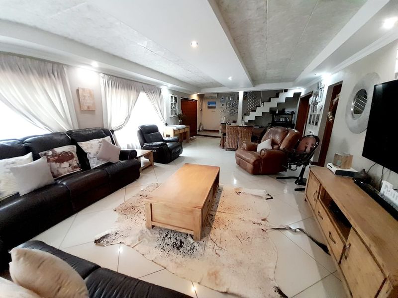 Spacious open-plan living area featuring tiled flooring, recessed ceiling lighting, and a staircase leading to the upper level.