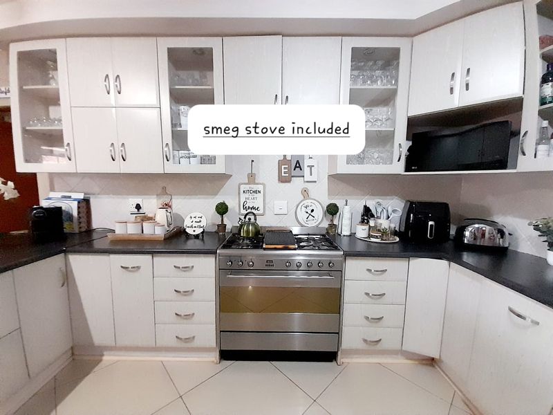 A well-maintained kitchen featuring white cabinetry, dark countertops, and a stainless steel Smeg gas stove with an integrated extractor fan.