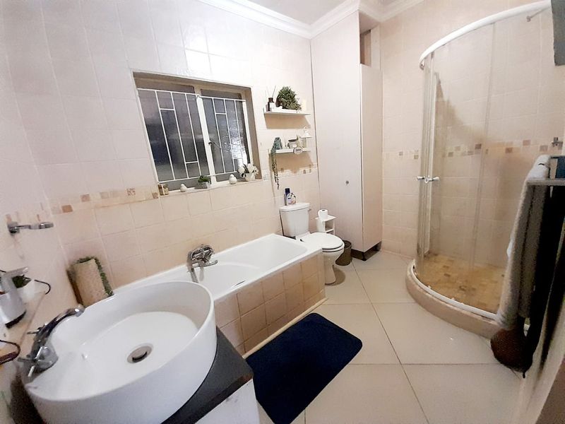 A functional bathroom featuring a corner shower enclosure, a built-in bathtub, a vanity basin, and a toilet with tiled walls and flooring.