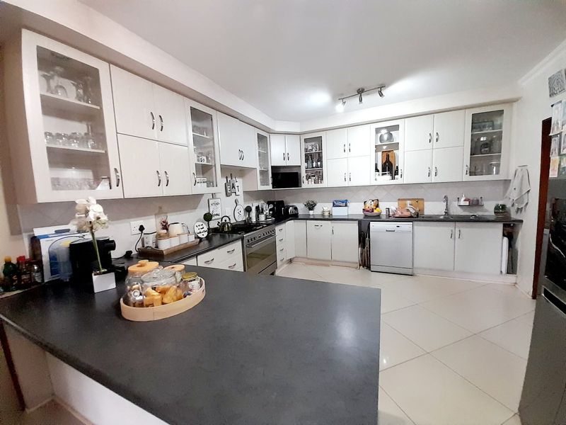 A well-maintained kitchen featuring white cabinetry, dark countertops, a built-in oven with gas hob, and tiled flooring.