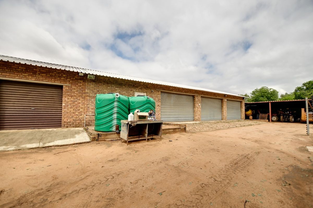 Exterior view of a large brick outbuilding featuring multiple roller shutter garage doors and external water storage tanks on a dirt yard.