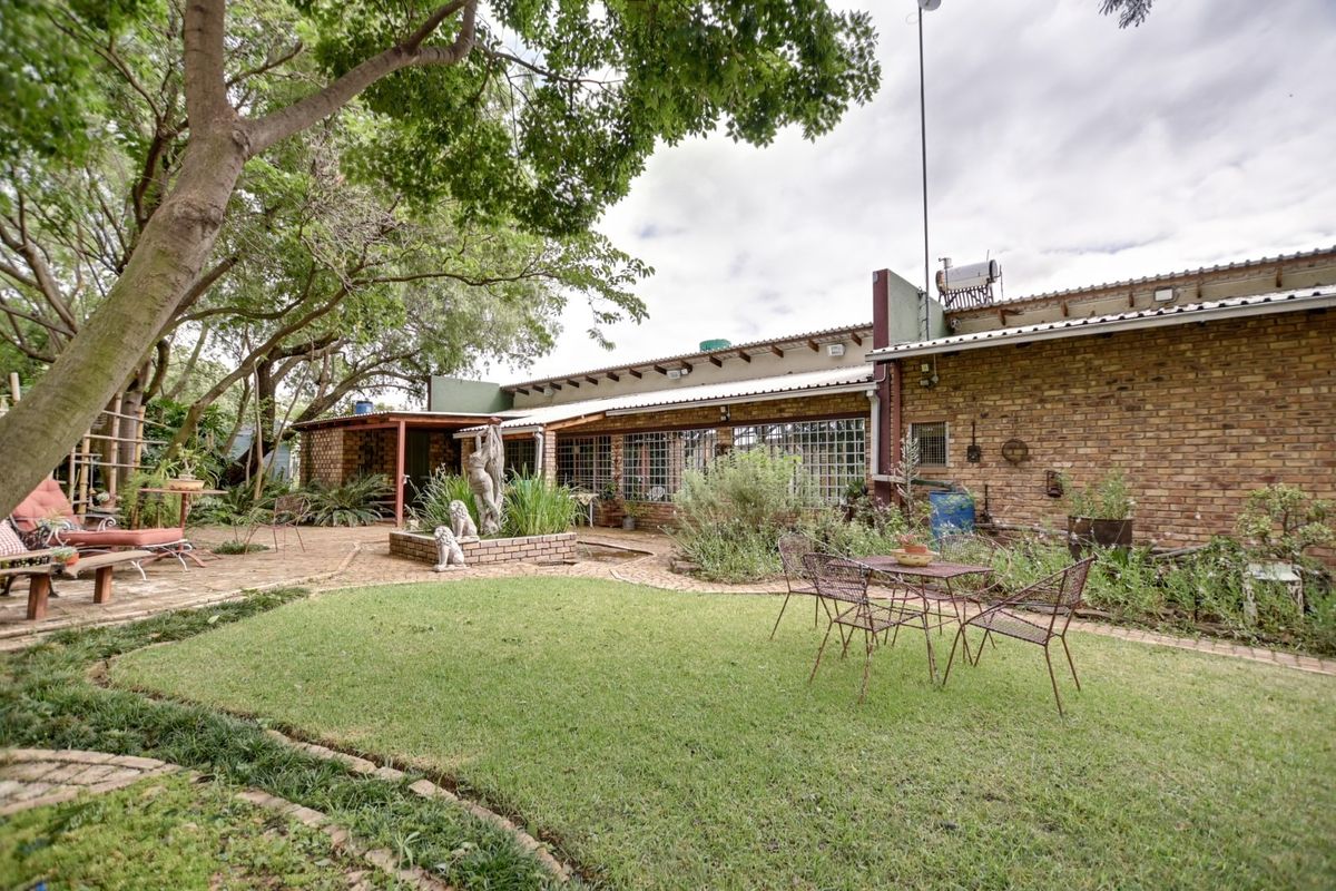 Rear view of the small holding featuring a face-brick facade, a paved patio area, and a landscaped garden with a built-in water feature.