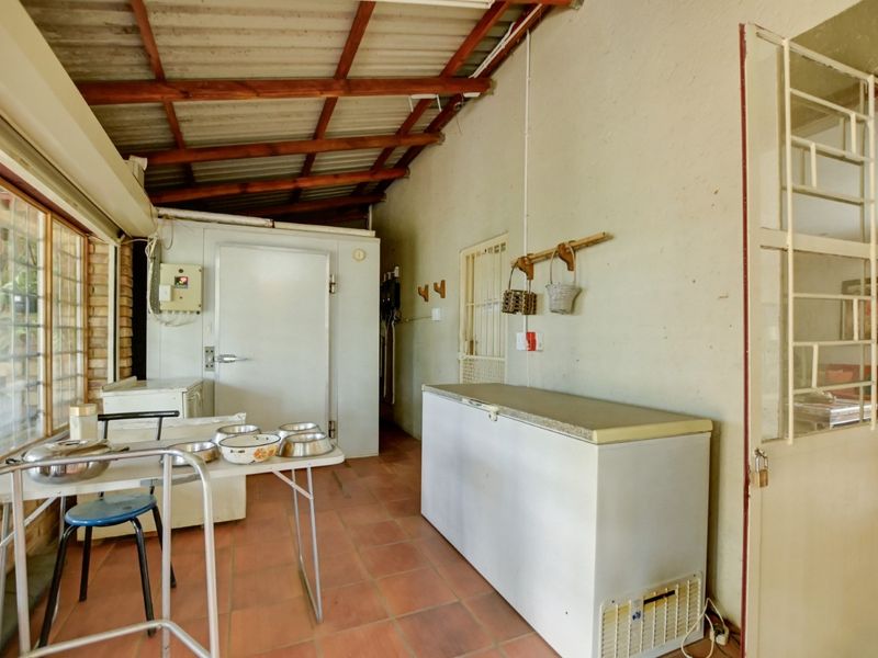 A functional scullery or utility area featuring tiled floors, exposed timber roof trusses, and a built-in cold storage unit.