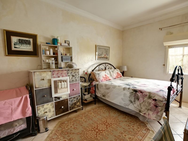 A bedroom featuring tiled flooring, coved ceiling cornices, and a wall-mounted air conditioning unit, currently showing signs of wall surface deterioration.