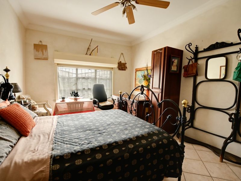 A well-proportioned bedroom featuring tiled flooring, a ceiling fan, and a window fitted with security bars.