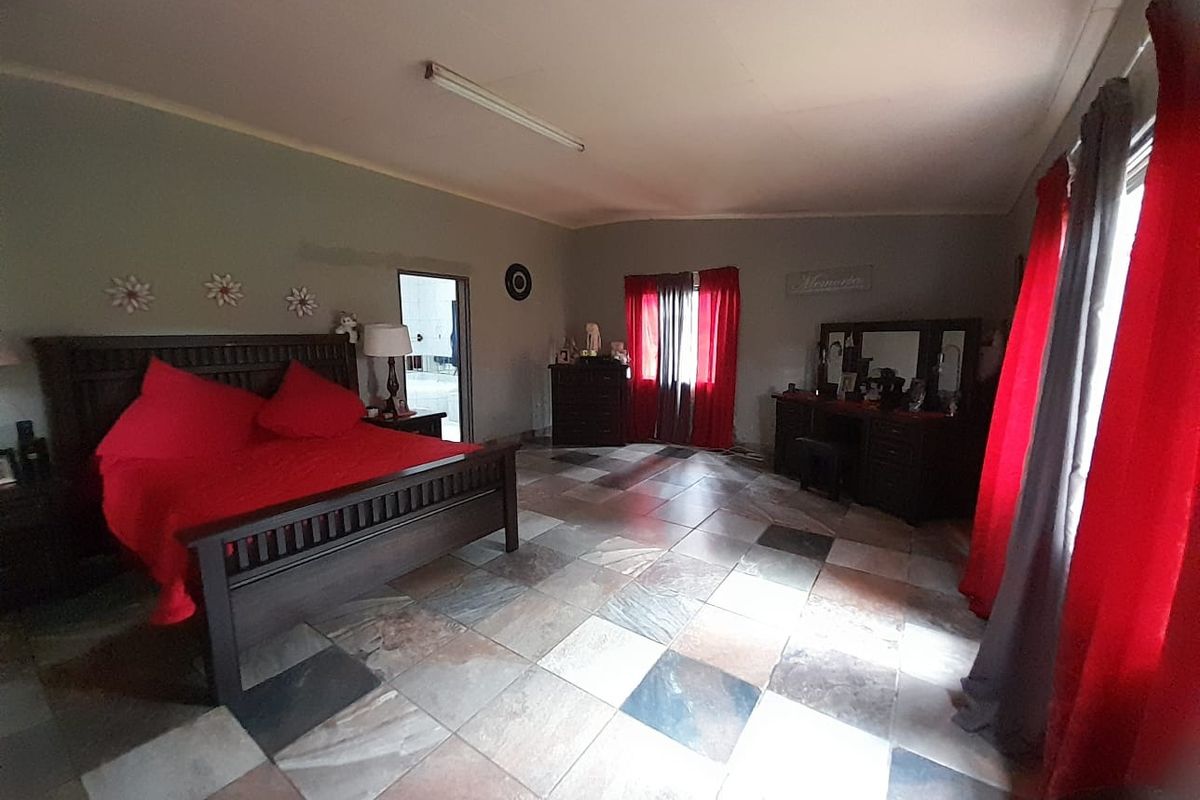 Spacious bedroom featuring large format multi-tonal floor tiles, neutral wall finishes, and natural light through window openings.