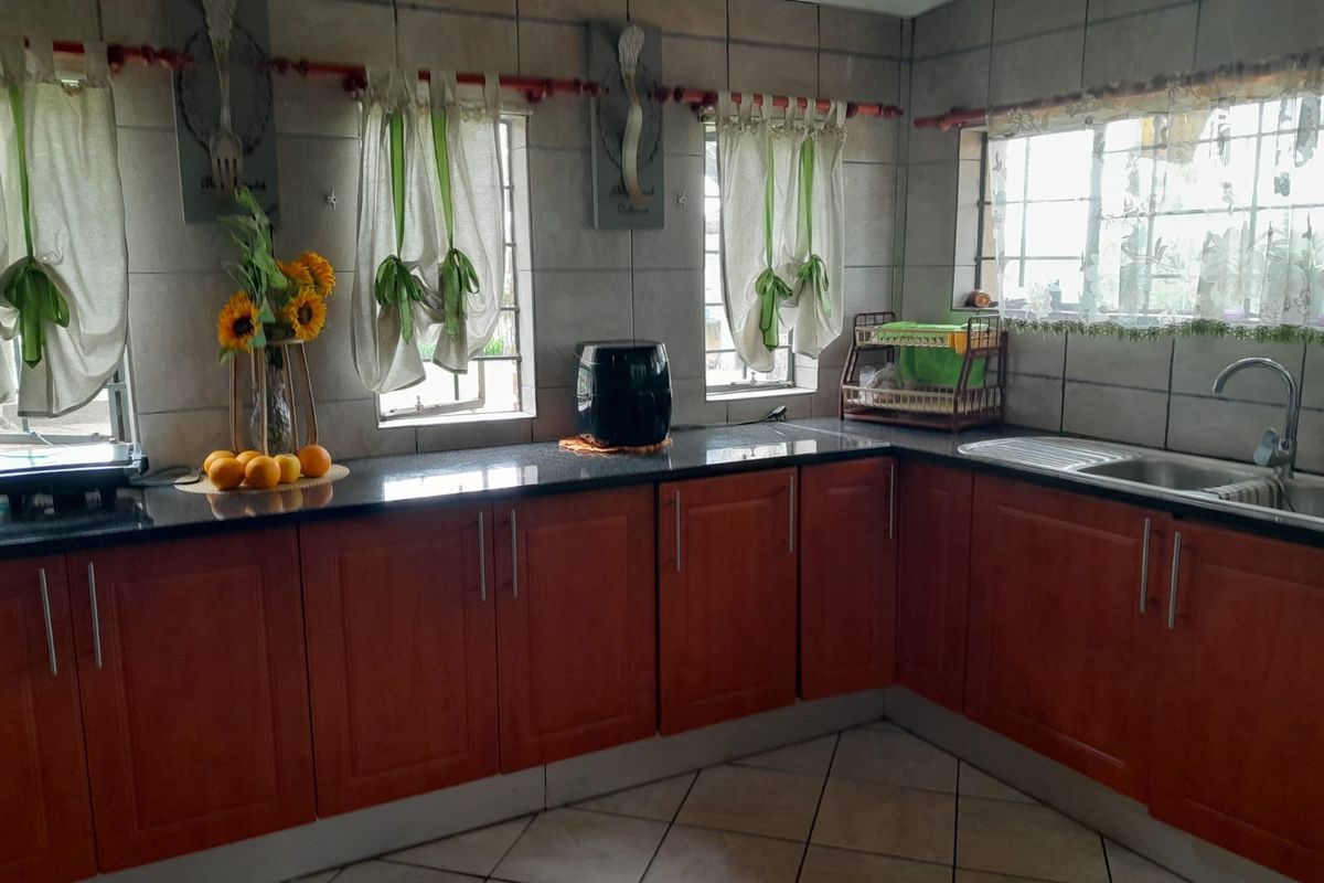 A functional kitchen featuring dark granite countertops, wooden cabinetry, tiled walls, and a stainless steel sink with a modern mixer tap.