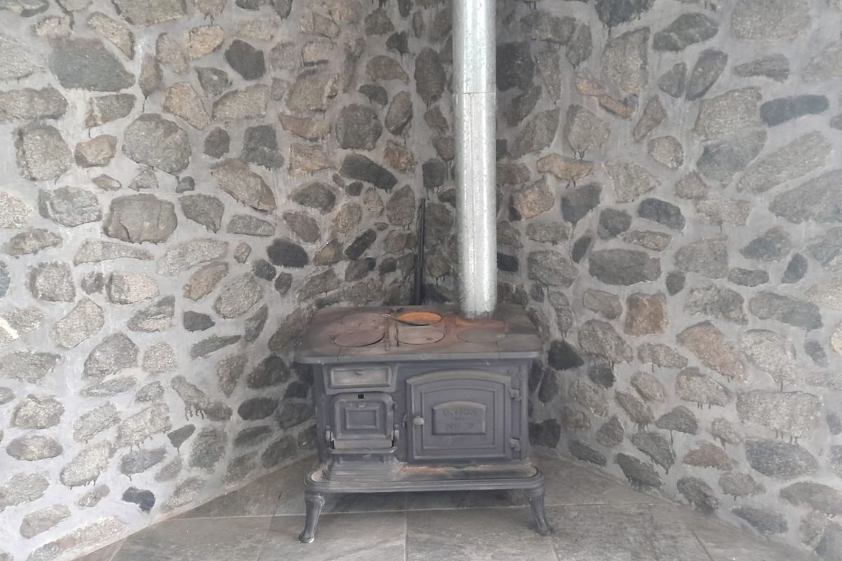 A rustic corner feature showcasing a vintage cast-iron wood-burning stove set against a natural stone wall with a metal flue pipe.
