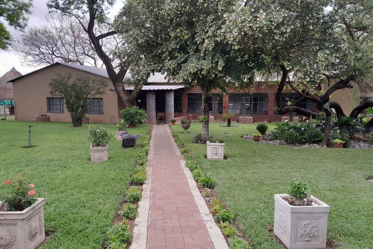 A well-maintained rear garden featuring a central brick paved walkway leading to the main dwelling with stone-clad pillars and security-fitted windows.