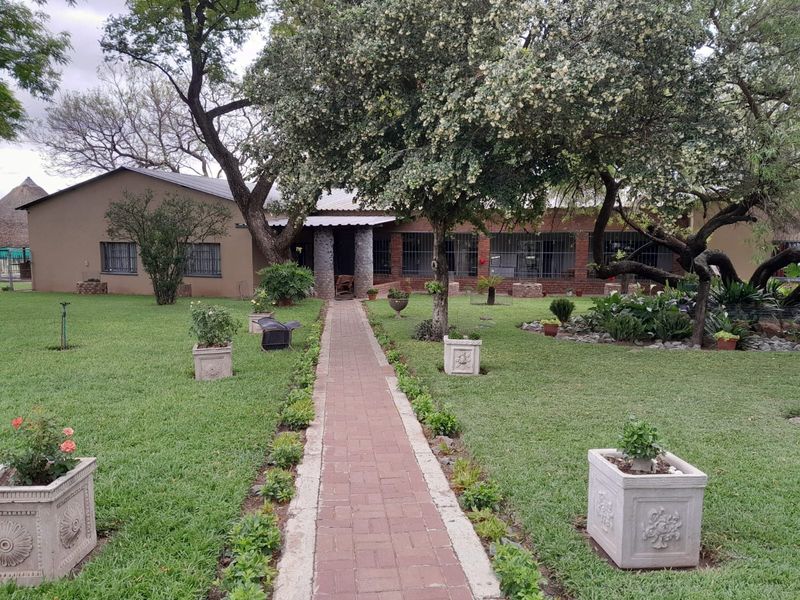 A well-maintained rear garden featuring a central brick paved walkway leading to the main dwelling with stone-clad pillars and security-fitted windows.