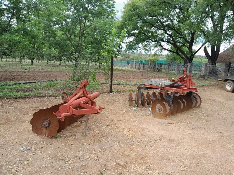 Outdoor garden area on a small holding featuring wire mesh fencing and an irrigation system, with agricultural equipment visible on the grounds.