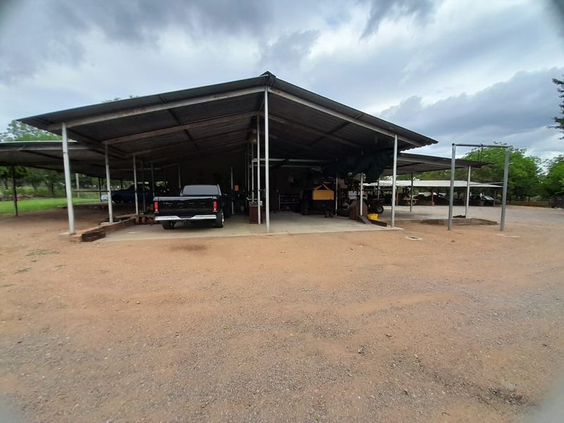 Large open-sided industrial-style garage or workshop structure with a metal roof and concrete flooring, suitable for vehicle storage or farm equipment maintenance.