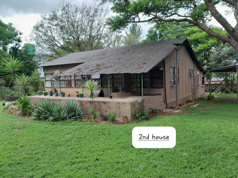 Rear view of a secondary dwelling featuring a covered patio, corrugated metal roofing, and established garden surroundings on a small holding property.