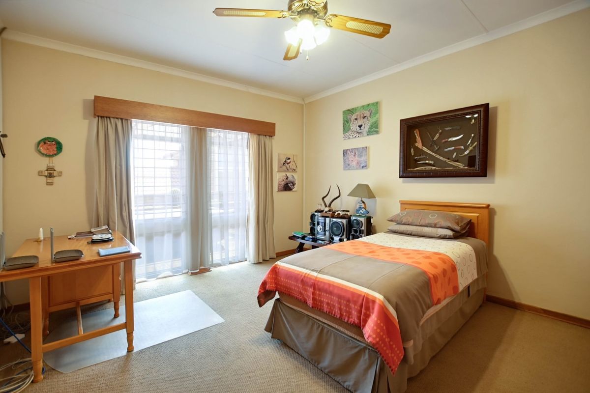 A well-maintained bedroom featuring neutral wall tones, carpeted flooring, a ceiling fan, and large sliding glass doors providing natural light.