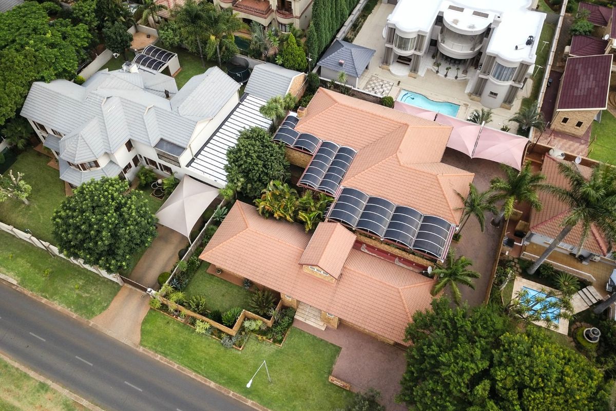 Aerial view of the property showcasing the tiled roof, extensive solar panel installation, landscaped garden, and paved driveway in a residential neighborhood.