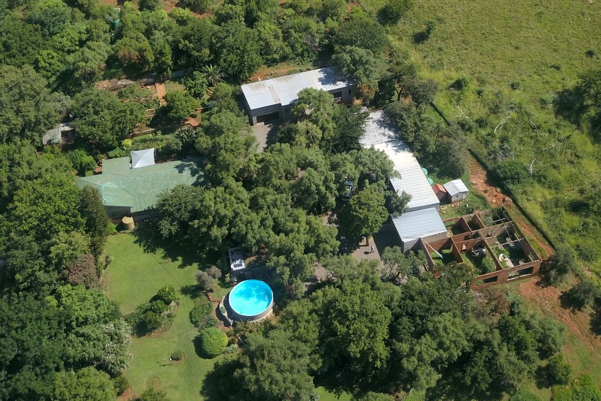 Aerial view of a farm property featuring multiple buildings, a swimming pool, mature trees, and an unfinished brick structure on the grounds.
