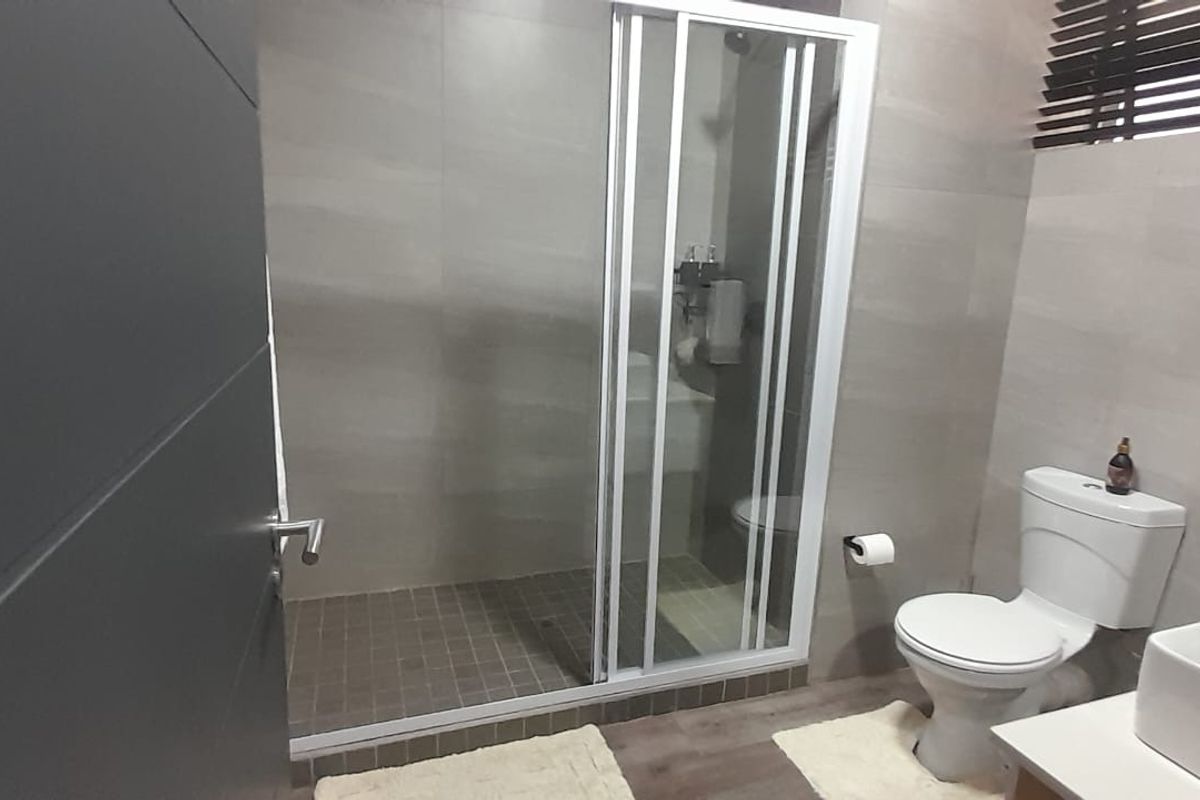 Modern bathroom featuring a walk-in shower with glass enclosure, a contemporary basin, and a toilet, finished with neutral wall tiles.