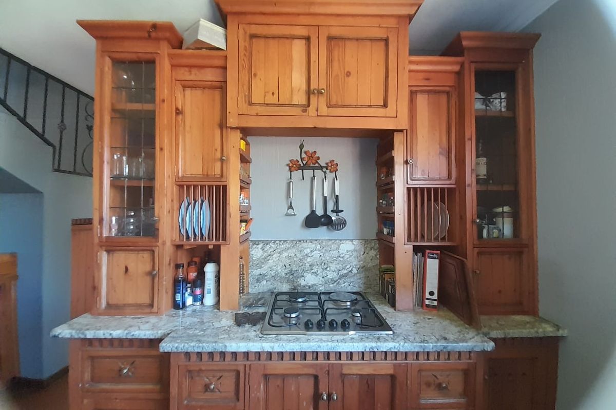 A rustic kitchen featuring solid wood cabinetry, granite countertops, and a built-in gas hob with integrated storage and display shelving.