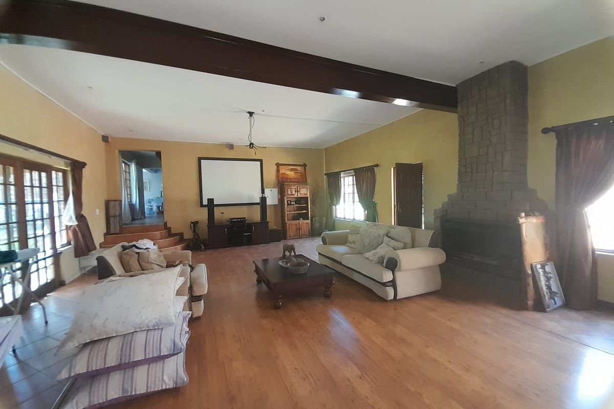 Spacious living room featuring a prominent stone-clad fireplace, exposed timber ceiling beams, and wooden flooring, offering a warm and inviting atmosphere.