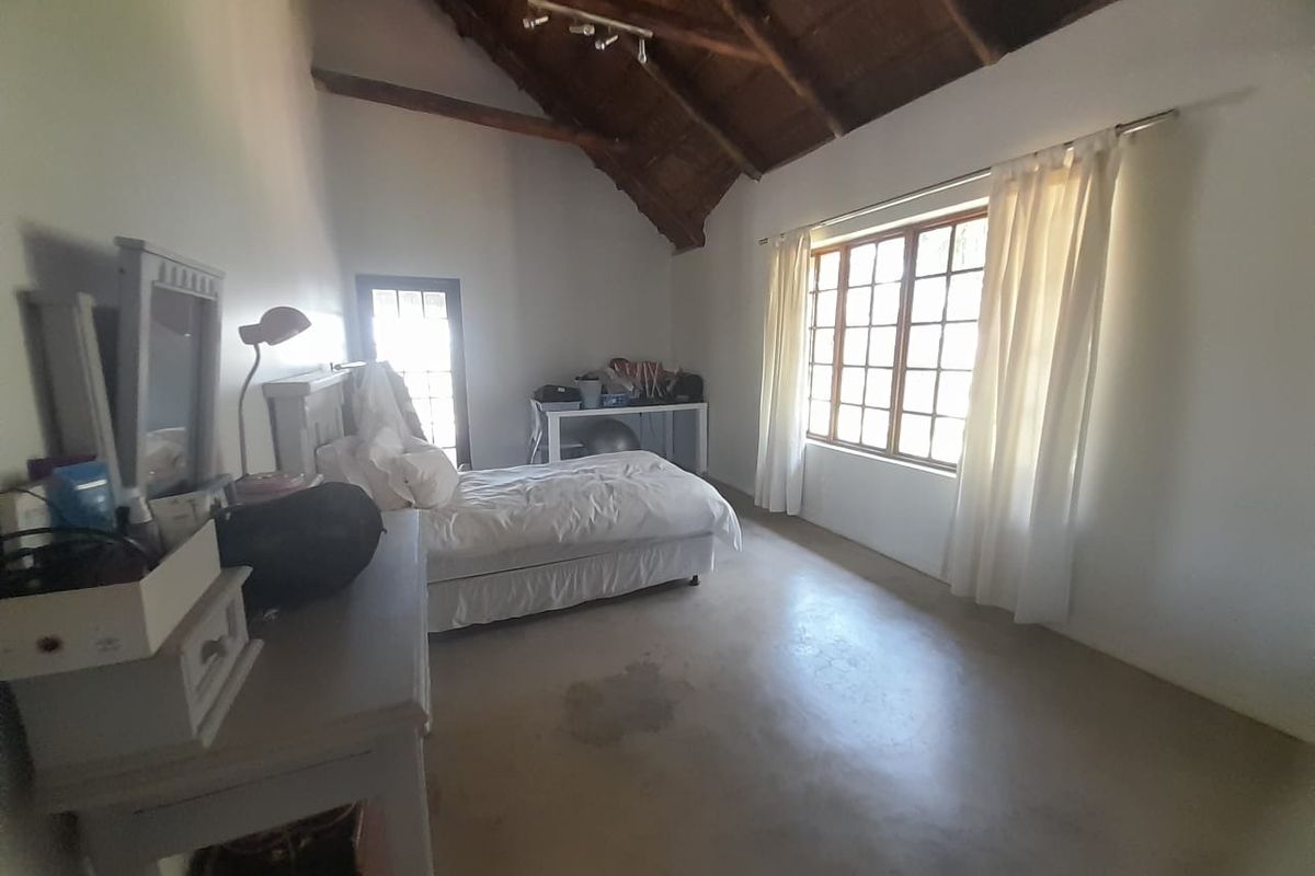Spacious bedroom featuring high vaulted ceilings with exposed timber beams, large windows, and polished concrete flooring.