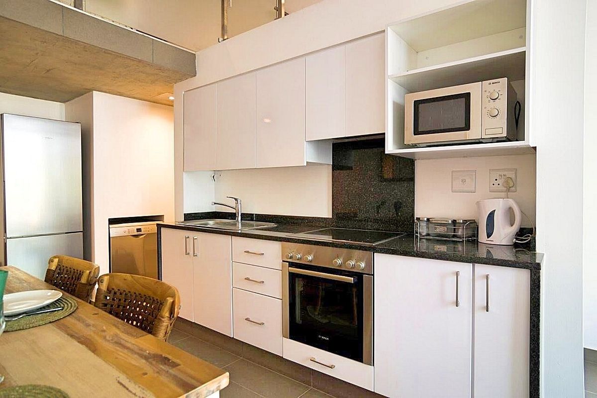 Modern kitchen featuring white cabinetry, granite countertops, integrated oven, hob, and built-in microwave, seamlessly flowing into the living area.