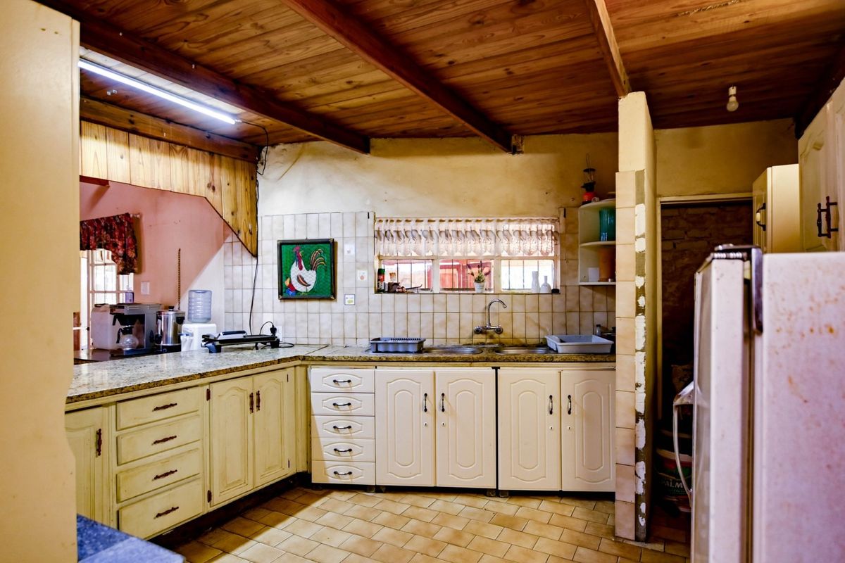 A dated kitchen featuring wooden ceiling beams, tiled countertops, and traditional cabinetry, offering a functional layout with potential for modernization.