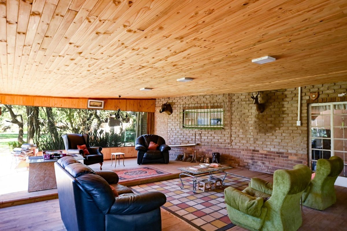 Spacious living area featuring a rustic exposed brick wall, timber-clad ceiling, and large windows providing natural light and garden views.