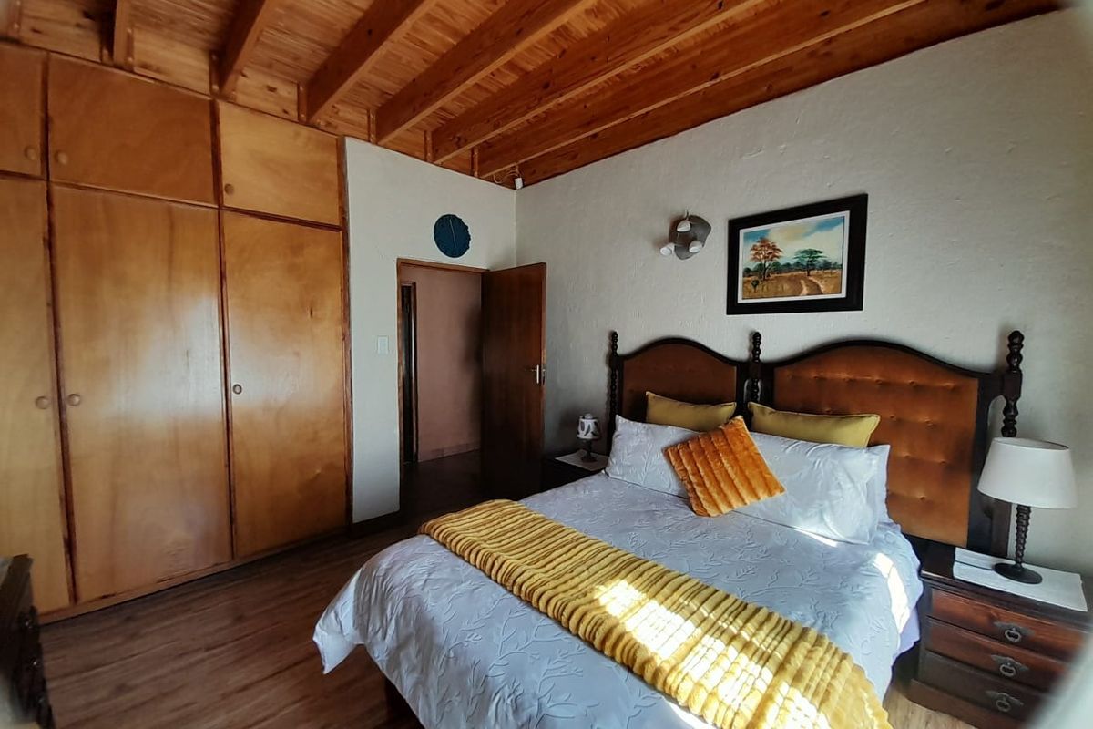 A bedroom featuring exposed wooden ceiling beams, built-in wooden cupboards, and laminate flooring.