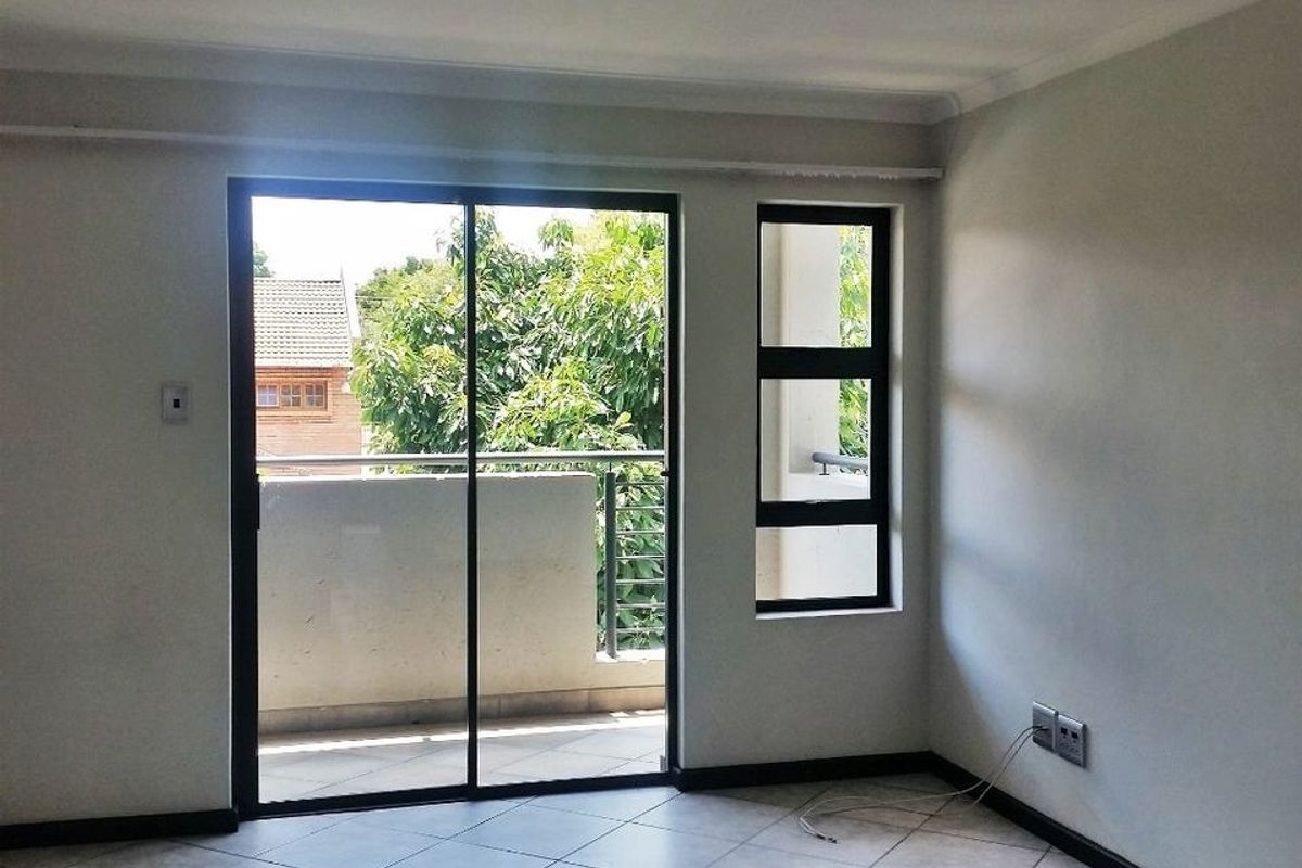 Bright living area featuring tiled flooring, black-framed sliding glass doors, and a large window providing access to an attached balcony.