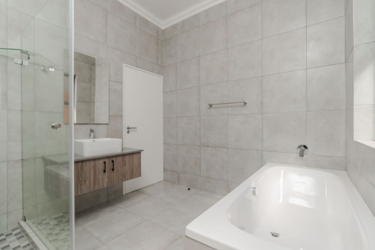 Modern bathroom featuring a glass-enclosed shower, a wall-mounted vanity with a vessel sink, and a built-in bathtub with neutral floor-to-ceiling tiling.