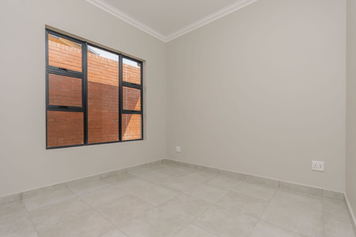 A clean, empty bedroom featuring neutral tiled flooring, modern black-framed windows, and crown molding, offering a bright and versatile living space.