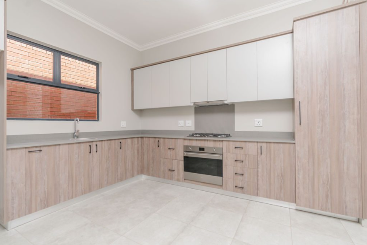 Modern kitchen featuring light wood-grain cabinetry, stone-look countertops, built-in oven, gas hob, extractor fan, and a stainless steel sink.