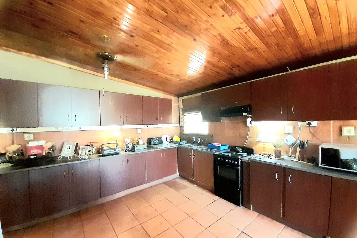 A functional kitchen featuring dark wood cabinetry, tiled flooring, and a distinctive wood-paneled ceiling with a built-in extractor fan.