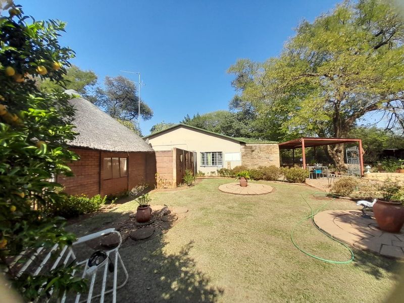Rear view of the property featuring a thatched roof section, brick and stone exterior finishes, a landscaped garden, and a covered outdoor patio area.