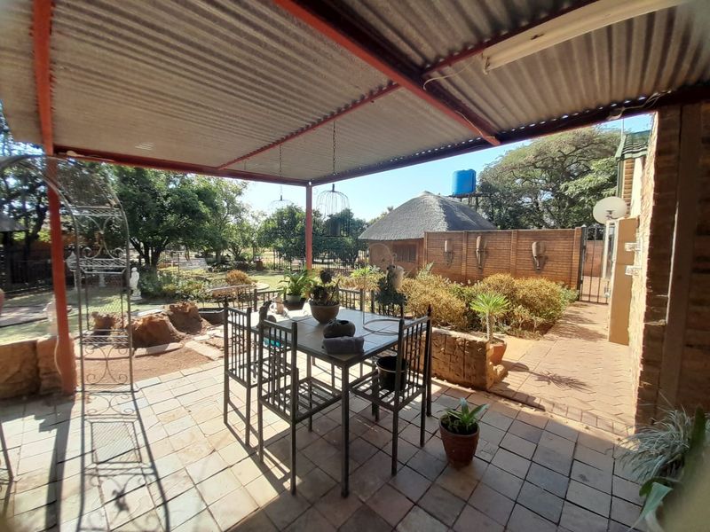 A covered outdoor patio area featuring paved flooring and a corrugated iron roof, overlooking a garden with a brick boundary wall.